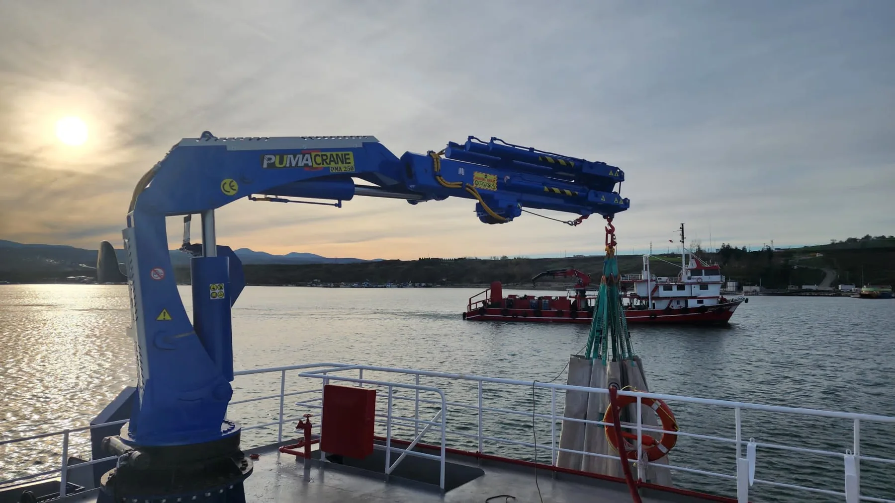 Blue marine crane installed on a vessel deck at sunset