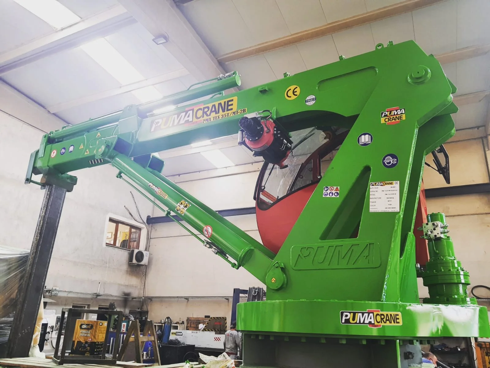 Green knuckle-boom marine crane prepared in a manufacturer workshop